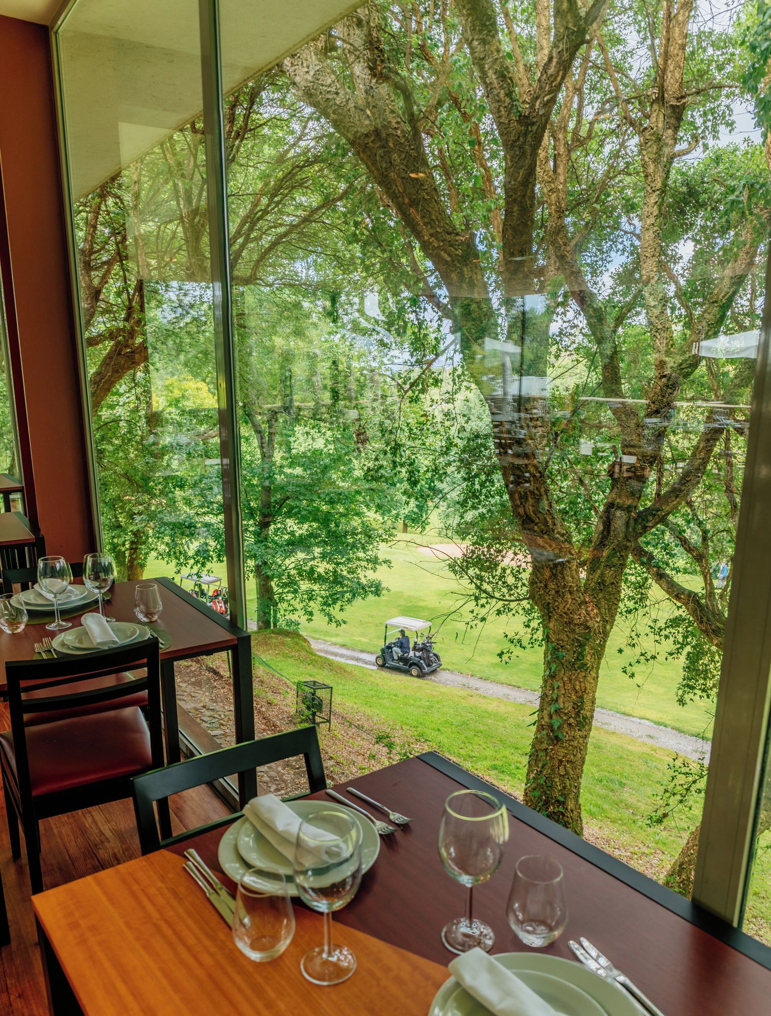 Área de jantar com mesa posta para quatro pessoas, amplas janelas com vista para um campo de golfe e árvores.