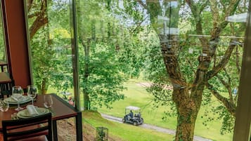 Área de jantar com mesa posta para quatro pessoas, amplas janelas com vista para um campo de golfe e árvores.