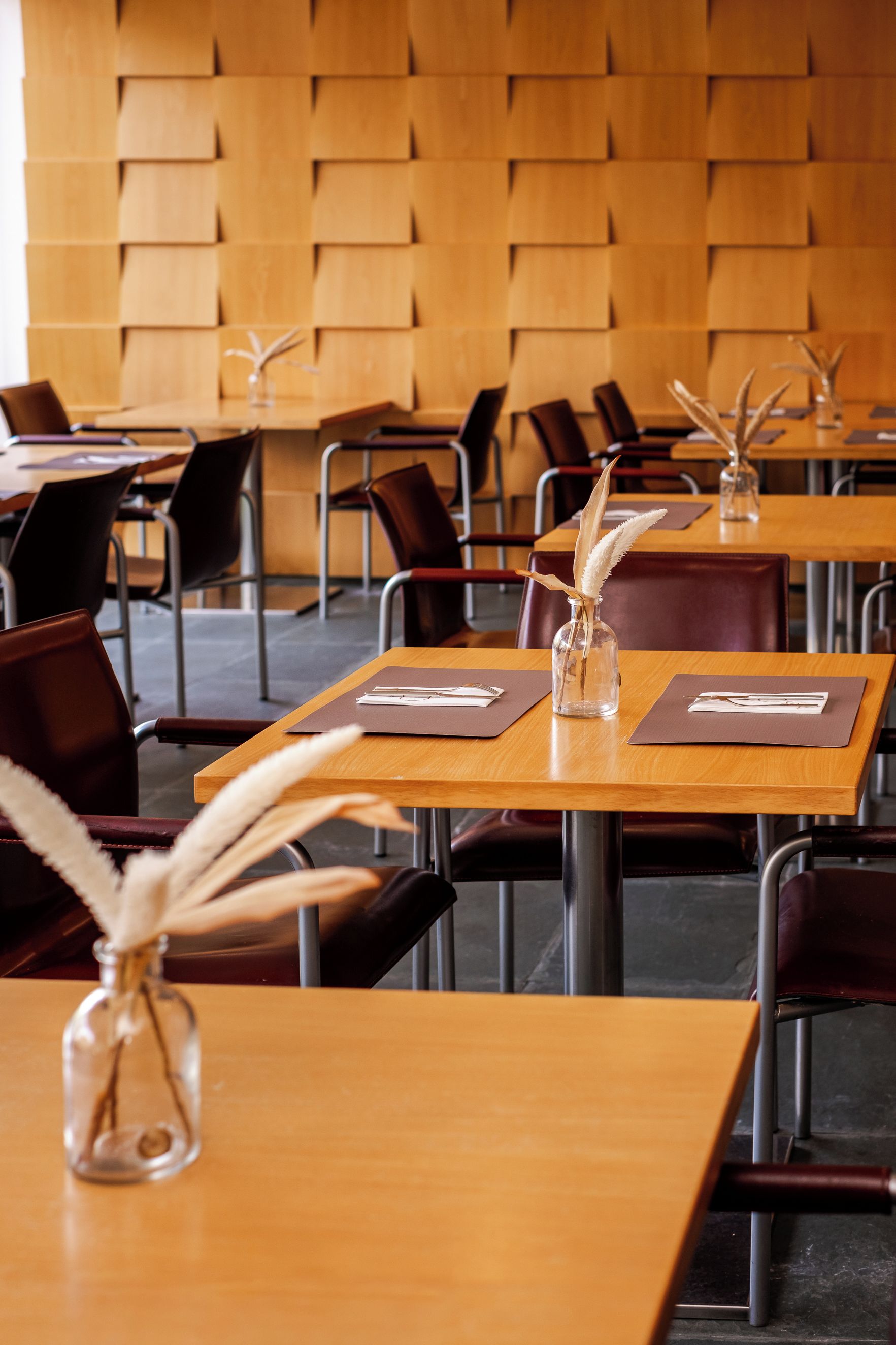 A conference room with wooden tables, chairs, and decorative vases with feathers.