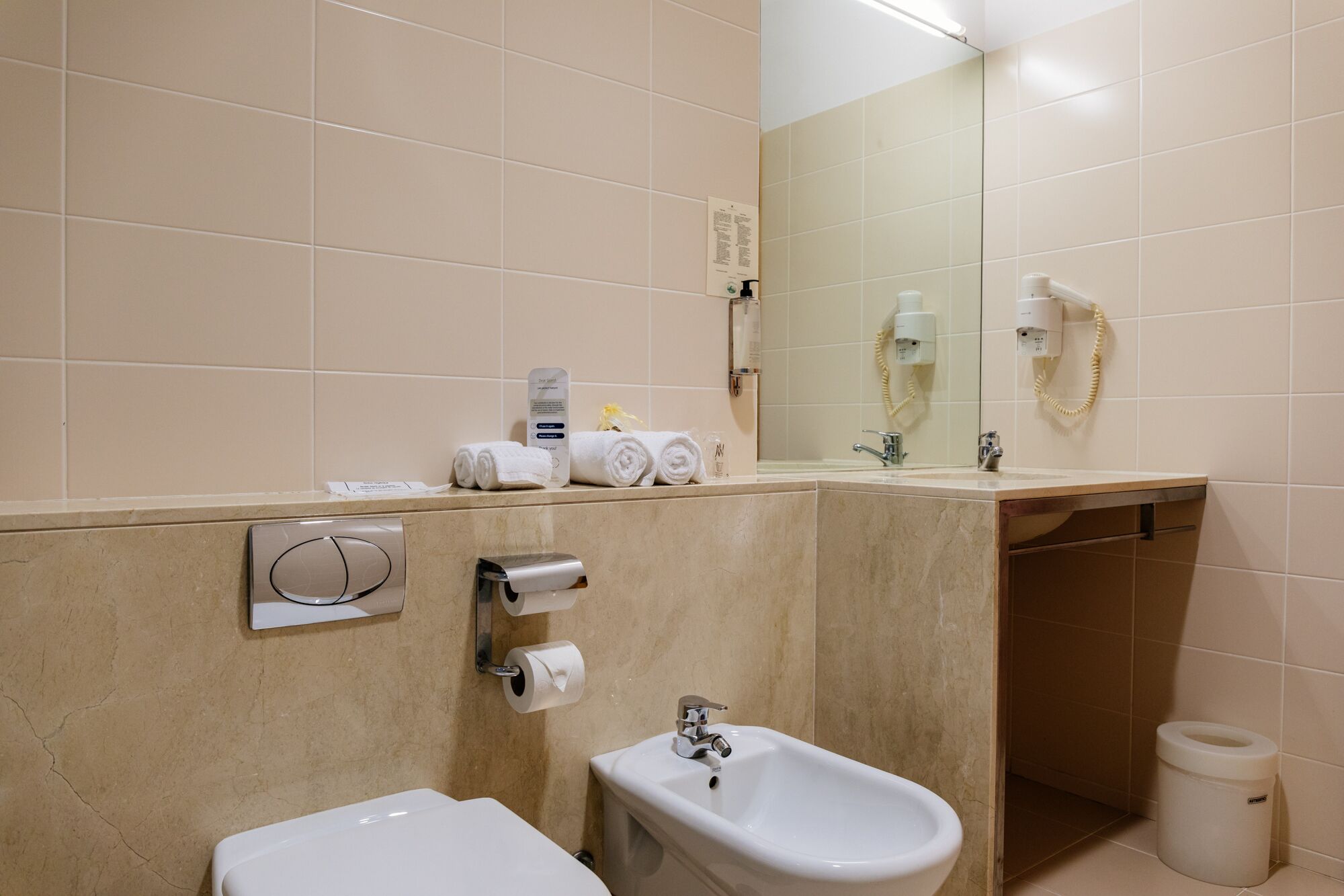 Un baño moderno con un bidé, un lavamanos y un espejo. Hay toallas y artículos de aseo en el mostrador.