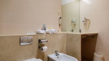 Een moderne badkamer met een bidet, een wastafel en een spiegel. Handdoeken en toiletartikelen liggen op het aanrecht.