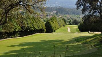 A golf course with a well-maintained fairway, a putting green, and a backdrop of trees and distant houses.