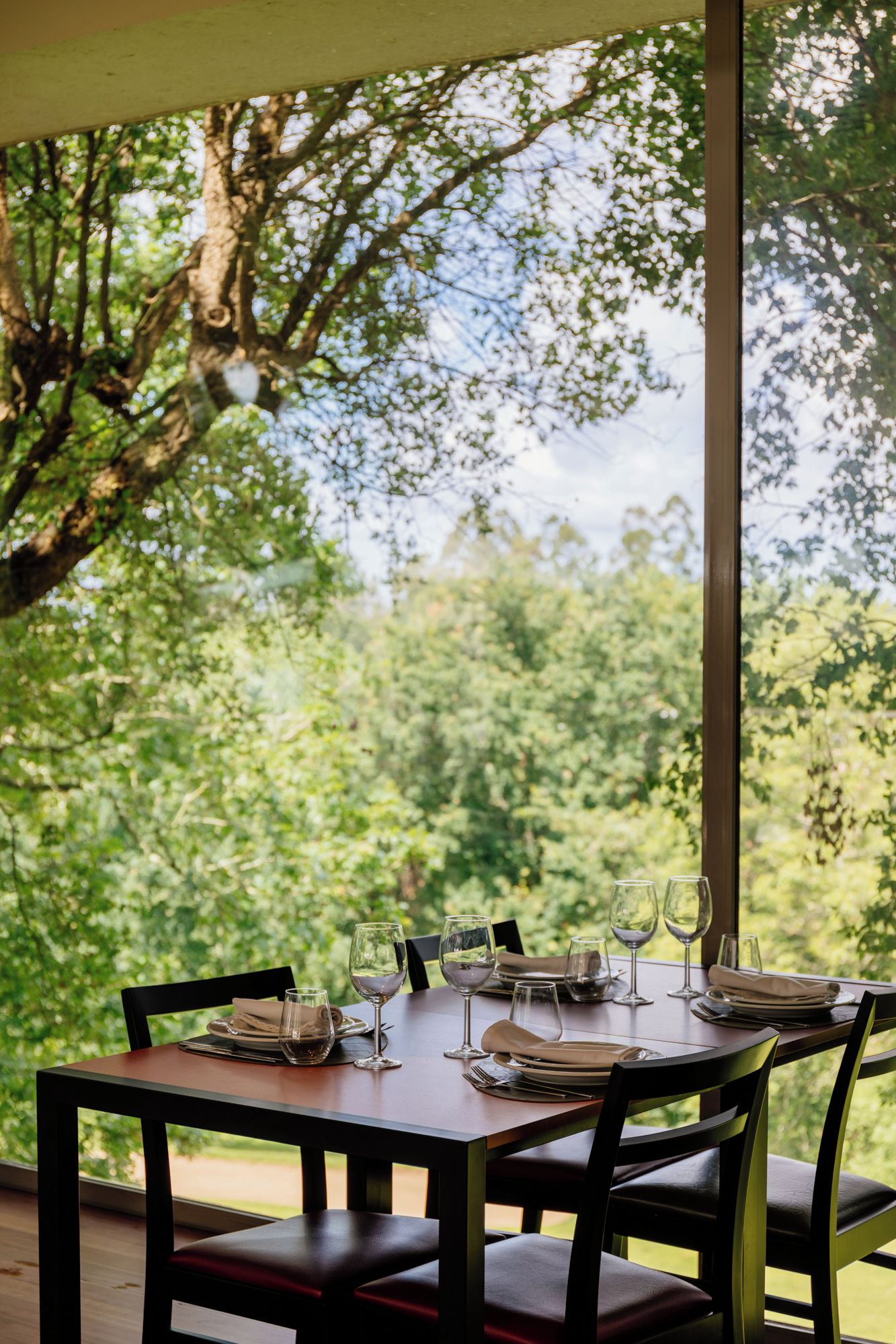 Un'area pranzo all'aperto con un tavolo apparecchiato per quattro persone, circondata da sedie e affacciata su un paesaggio boschivo.