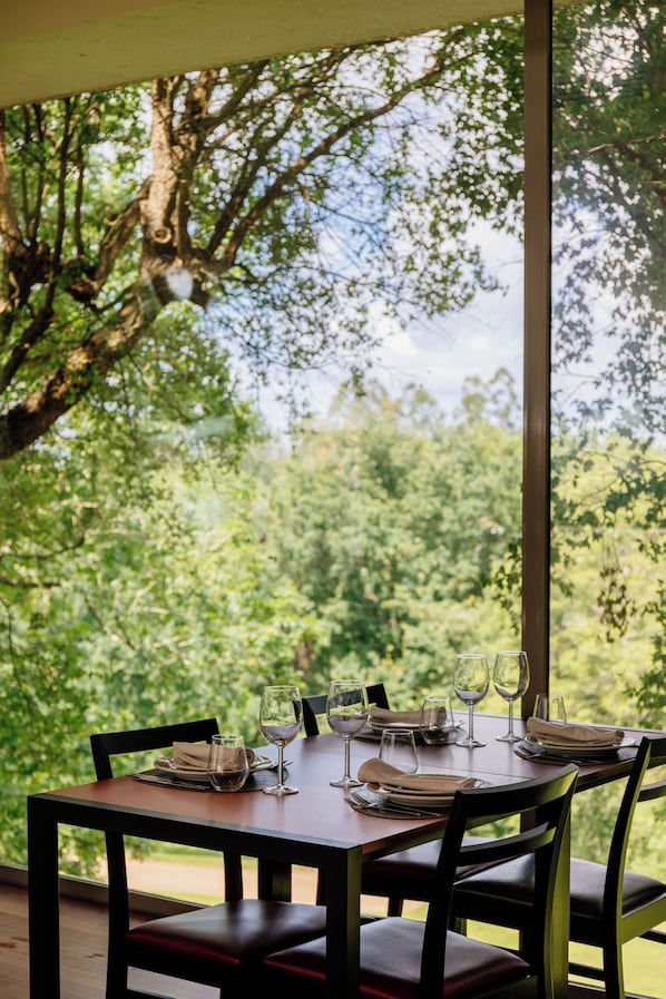 Un espace de restauration en plein air avec une table dressée pour quatre personnes, entourée de chaises, et offrant une vue sur un paysage boisé.