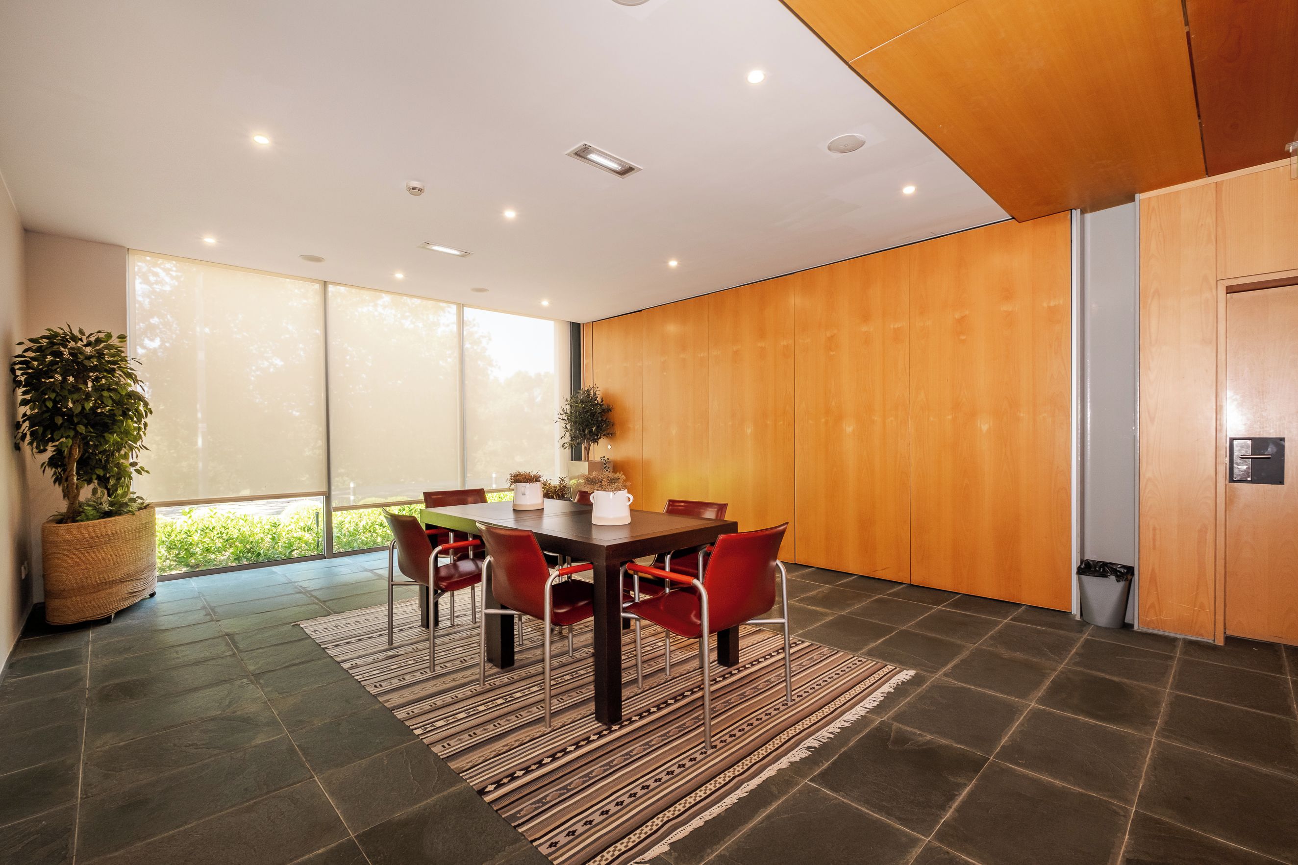 A modern dining area with a wooden table, red chairs, and a large window.
