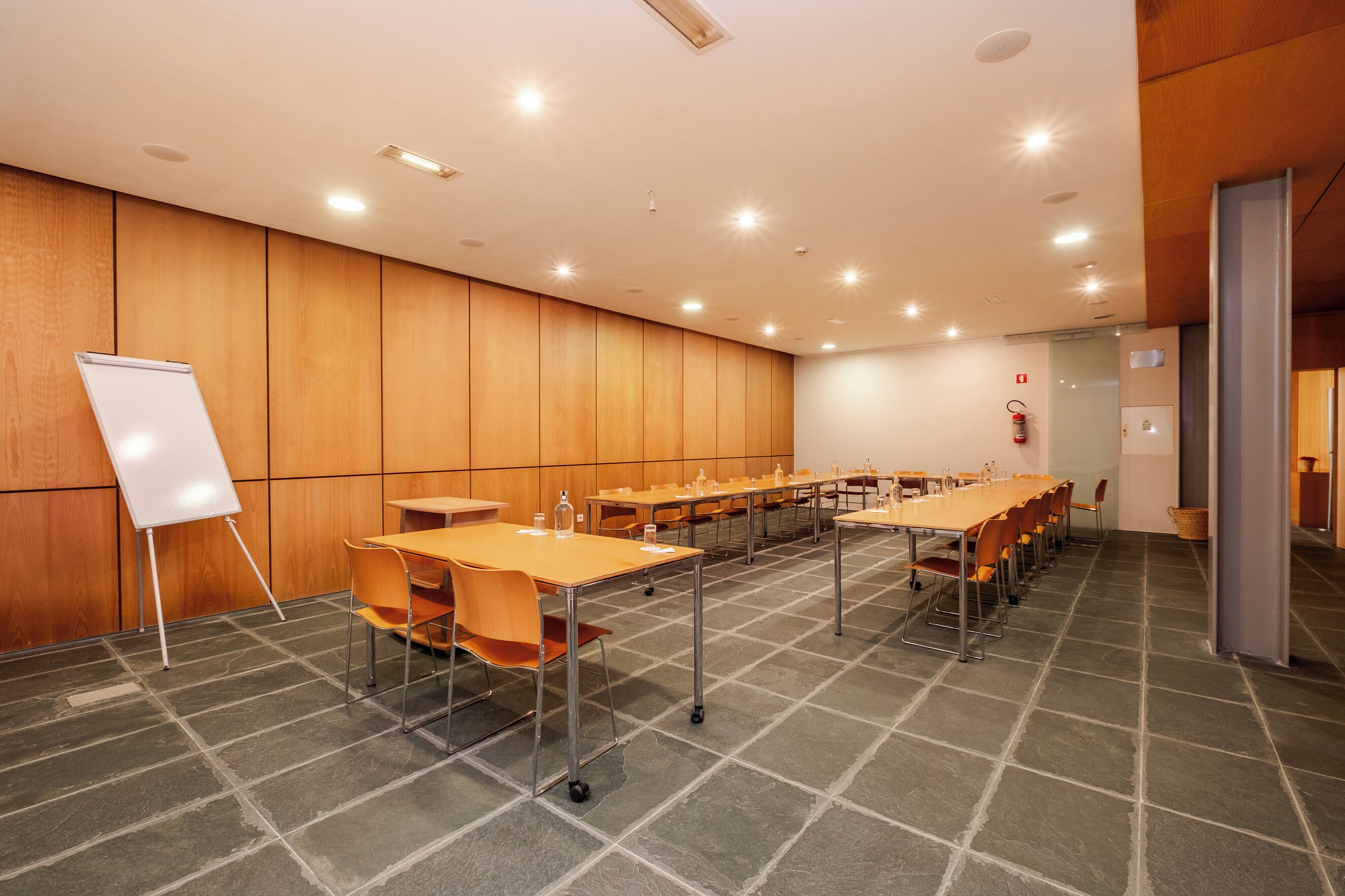 Un salón de conferencias con mesas largas, sillas, una pizarra y un extintor.