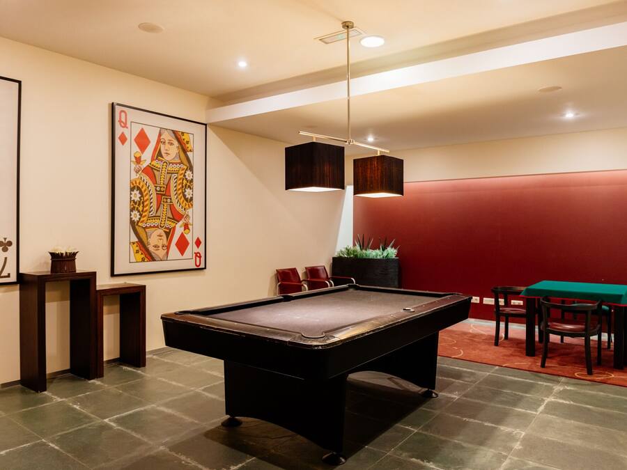 A billiards table in a room with a red accent wall, a large framed playing card, and a potted plant.