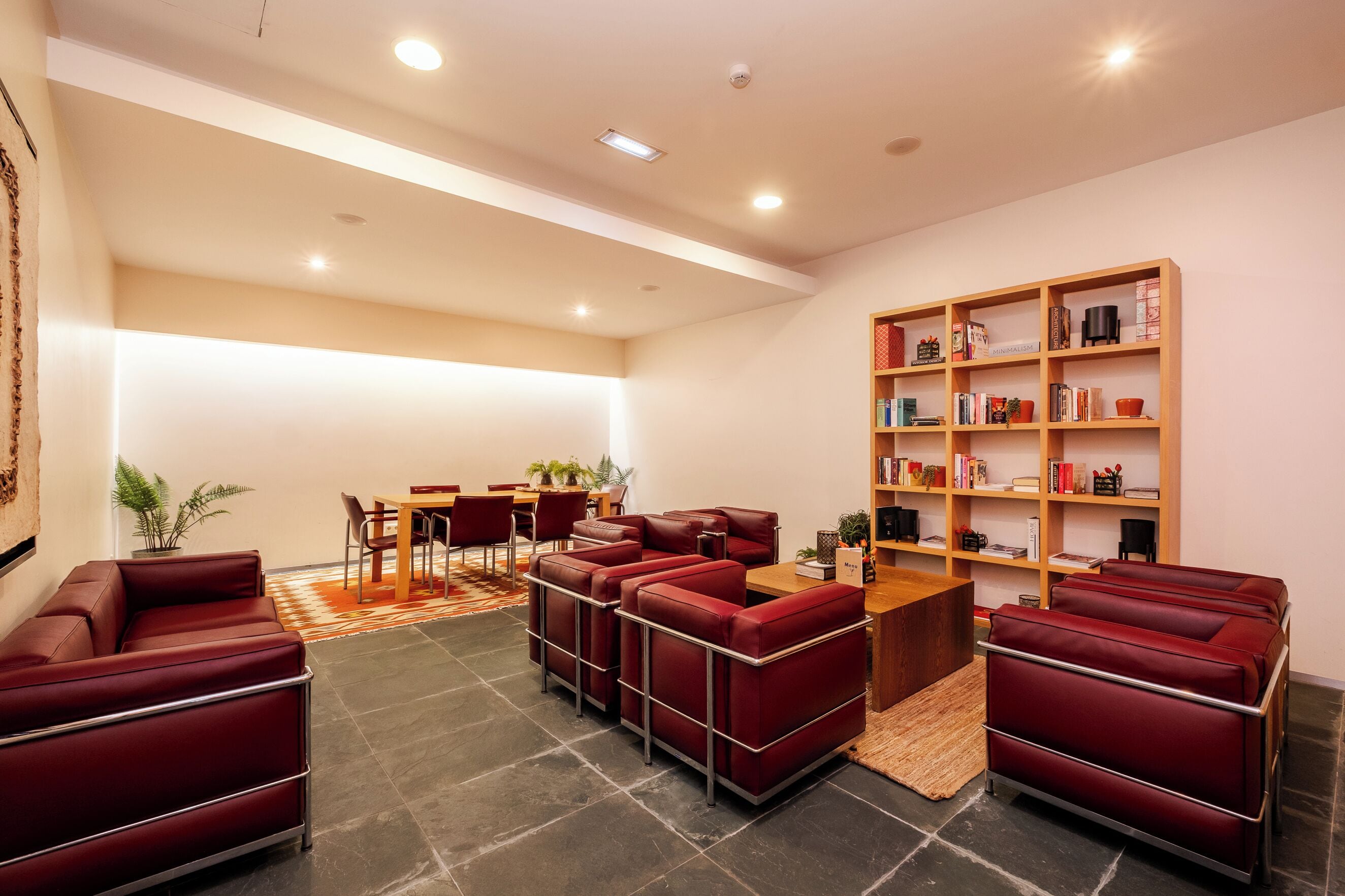 Ein moderner Lounge-Bereich mit roten Ledersofas, einem Holzregal und einem Essbereich mit Tisch und Stühlen.