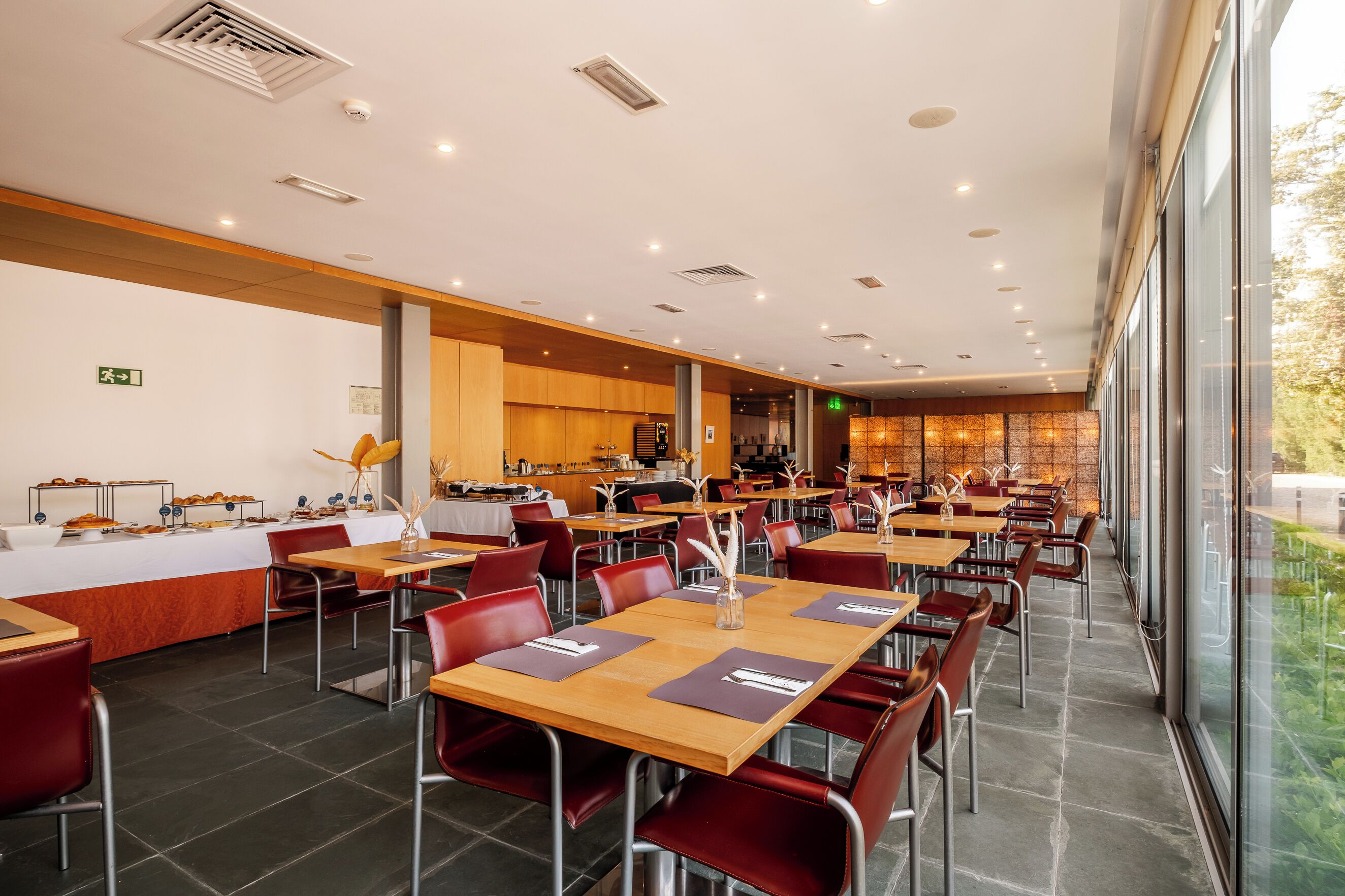 Un'ampia sala da pranzo con numerosi tavoli e sedie, un banco buffet e vista sull'esterno attraverso ampie finestre.