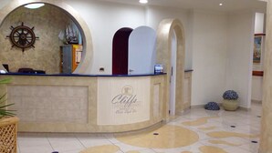 A hotel reception area with a curved counter, a ship's wheel on the wall, and a tiled floor with a geometric pattern. - Cliffs Hotel (Joppolo)