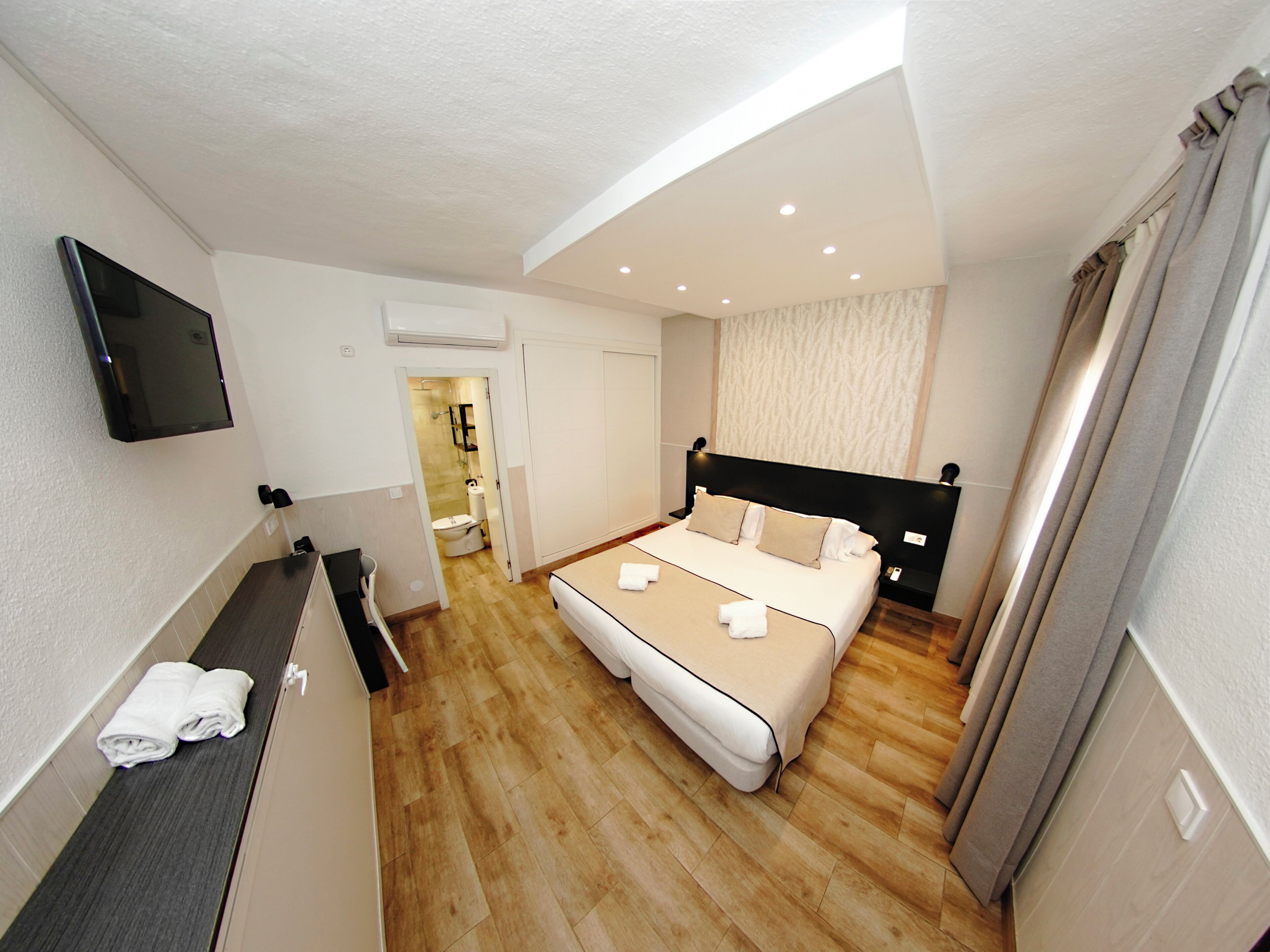 Habitación de hotel con cama, televisor montado en la pared y baño visible a través de una puerta abierta.