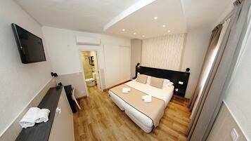 Habitación de hotel con cama, televisor montado en la pared y baño visible a través de una puerta abierta.