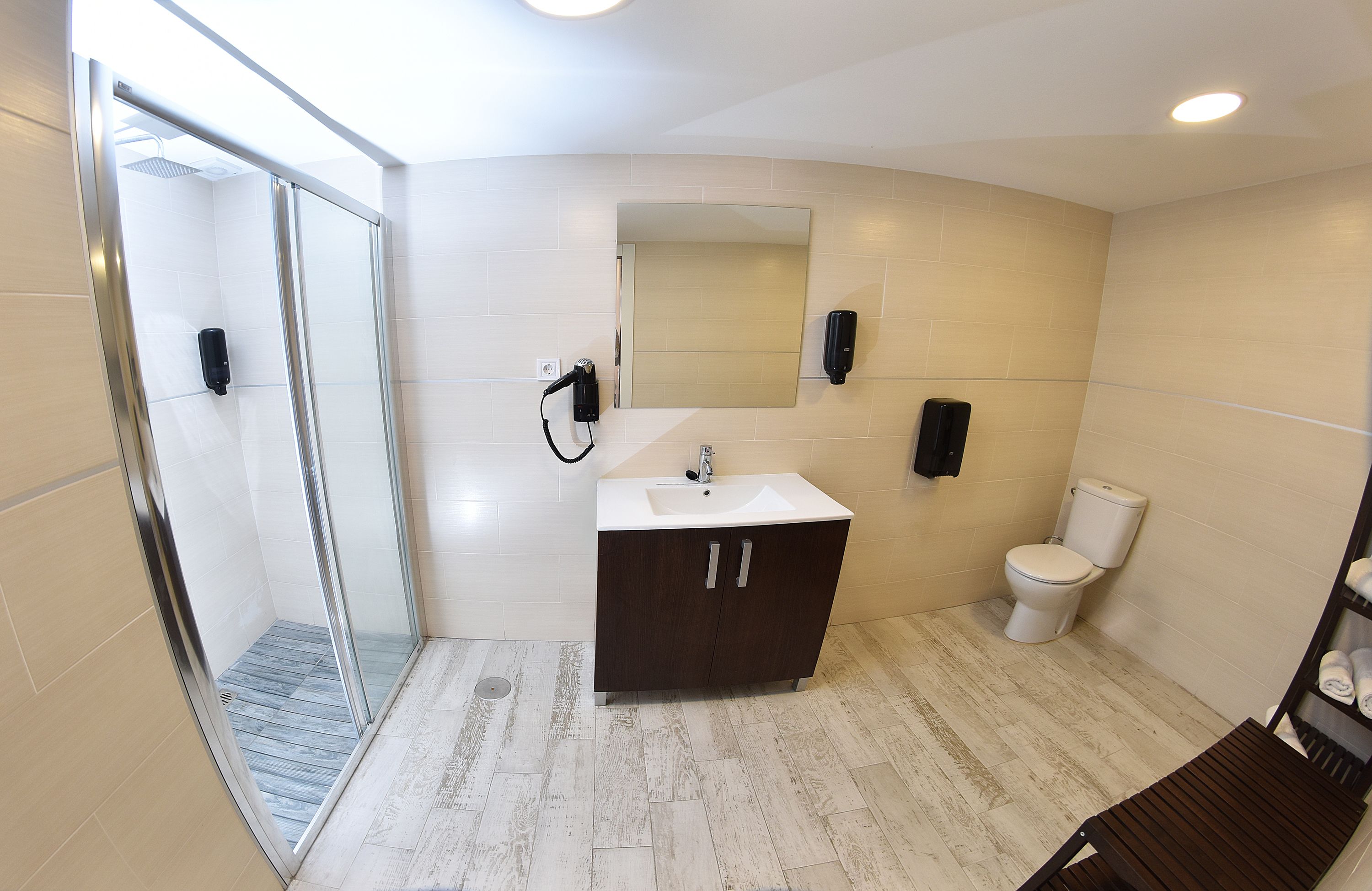 Un baño moderno con cabina de ducha de vidrio, lavamanos blanco, mueble de madera oscura y retrete blanco.