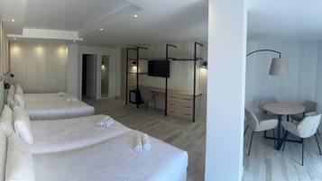 A modern hotel room with a large bed, a desk, a TV, and a dining area.