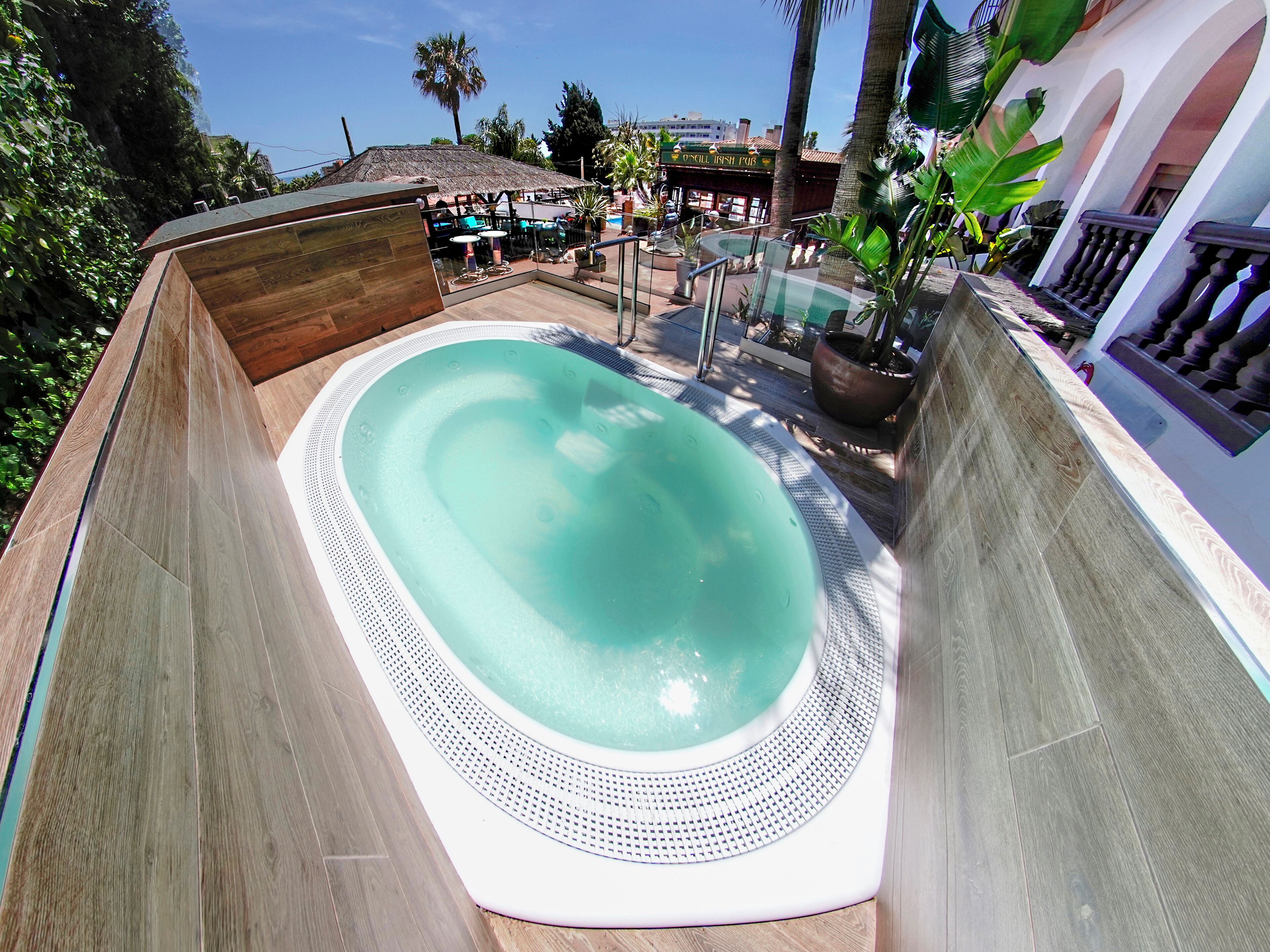 A hot tub surrounded by a wooden deck, with a pool table and a bar area in the background.
