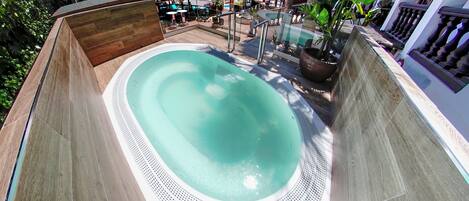A hot tub surrounded by a wooden deck, with a pool table and a bar area in the background.