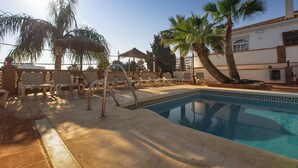 A pool area with lounge chairs, a pool with decorative tiles, palm trees, and a building in the background. - Hotel Zen Airport with Free shuttle (Torremolinos)