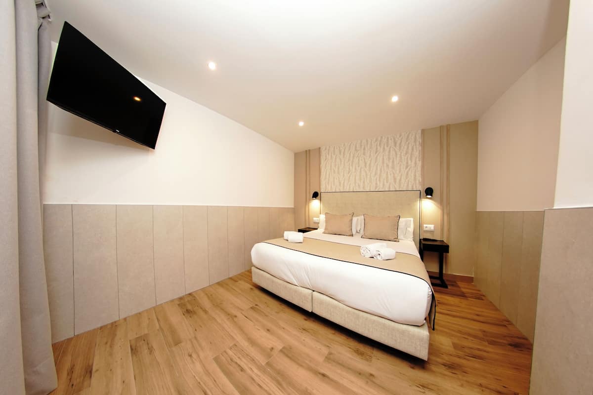 A modern hotel room with a large bed, a flat-screen TV mounted on the wall, and a wooden floor.