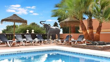 Un área de piscina con sillas de descanso, una gran estatua de elefante y palmeras.