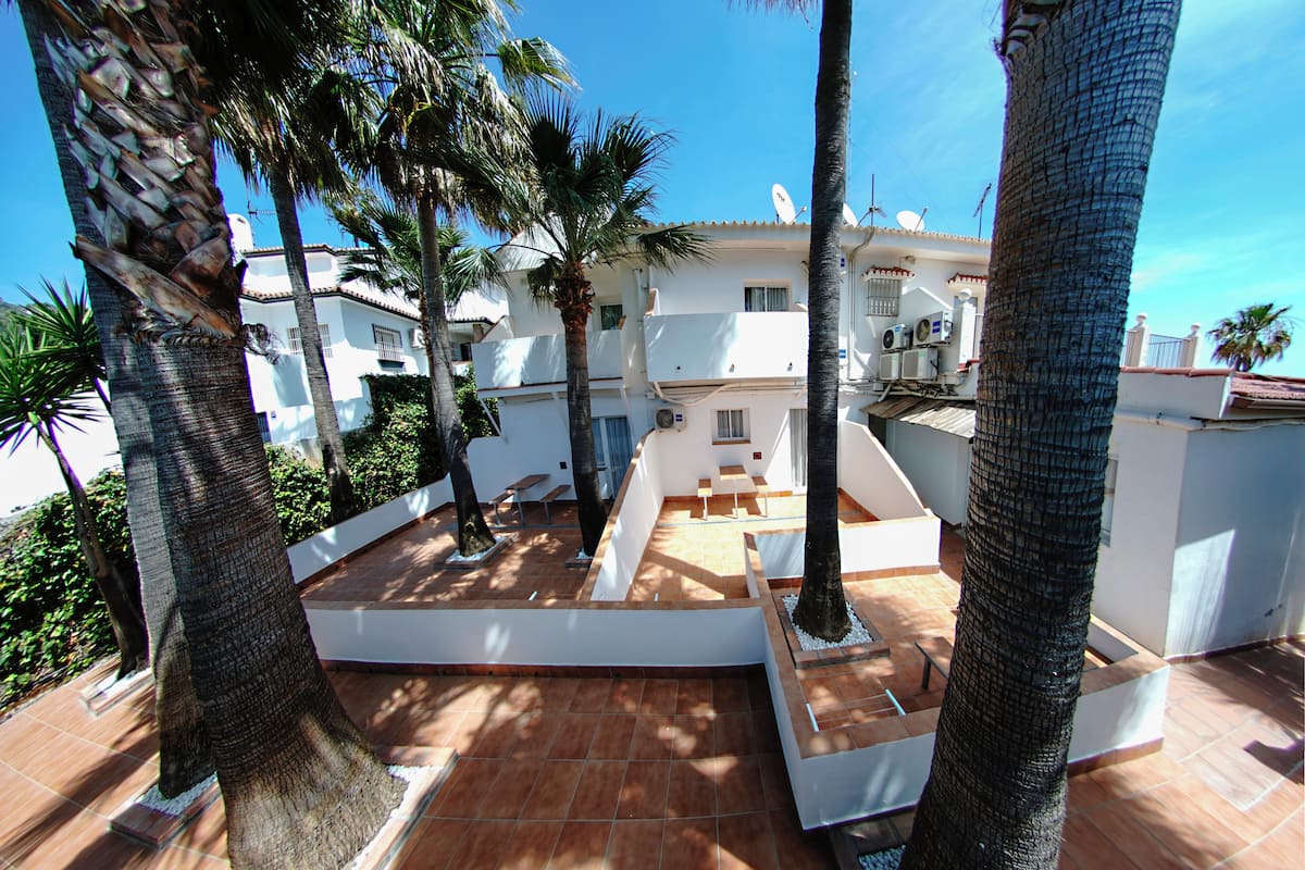 A courtyard with palm trees, a tiled floor, and a white building with balconies.