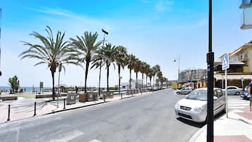 Une rue côtière bordée de palmiers, avec une plage en arrière-plan.