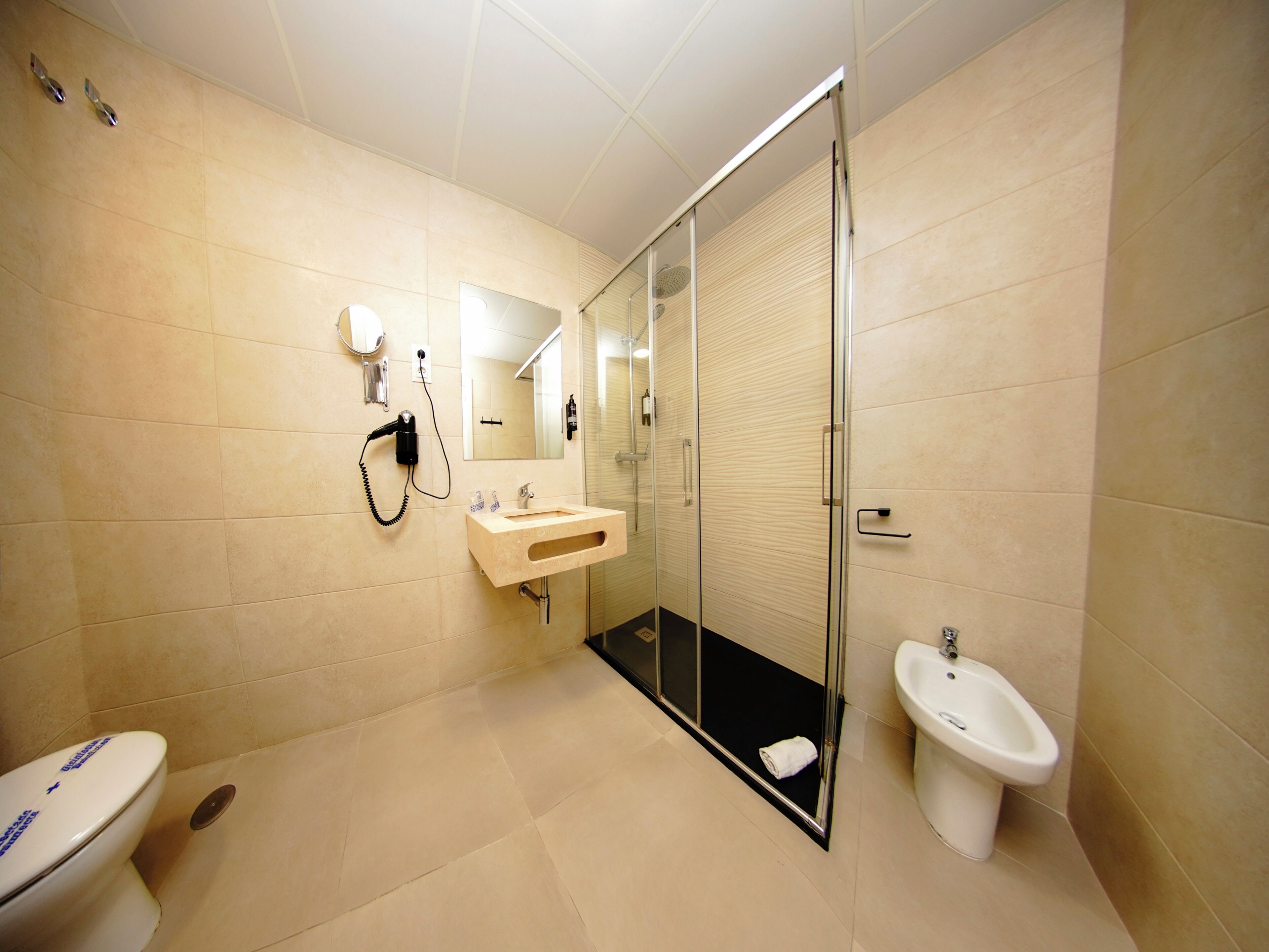 Un baño moderno con inodoro, lavamanos, bidé y zona de ducha con mampara de vidrio.