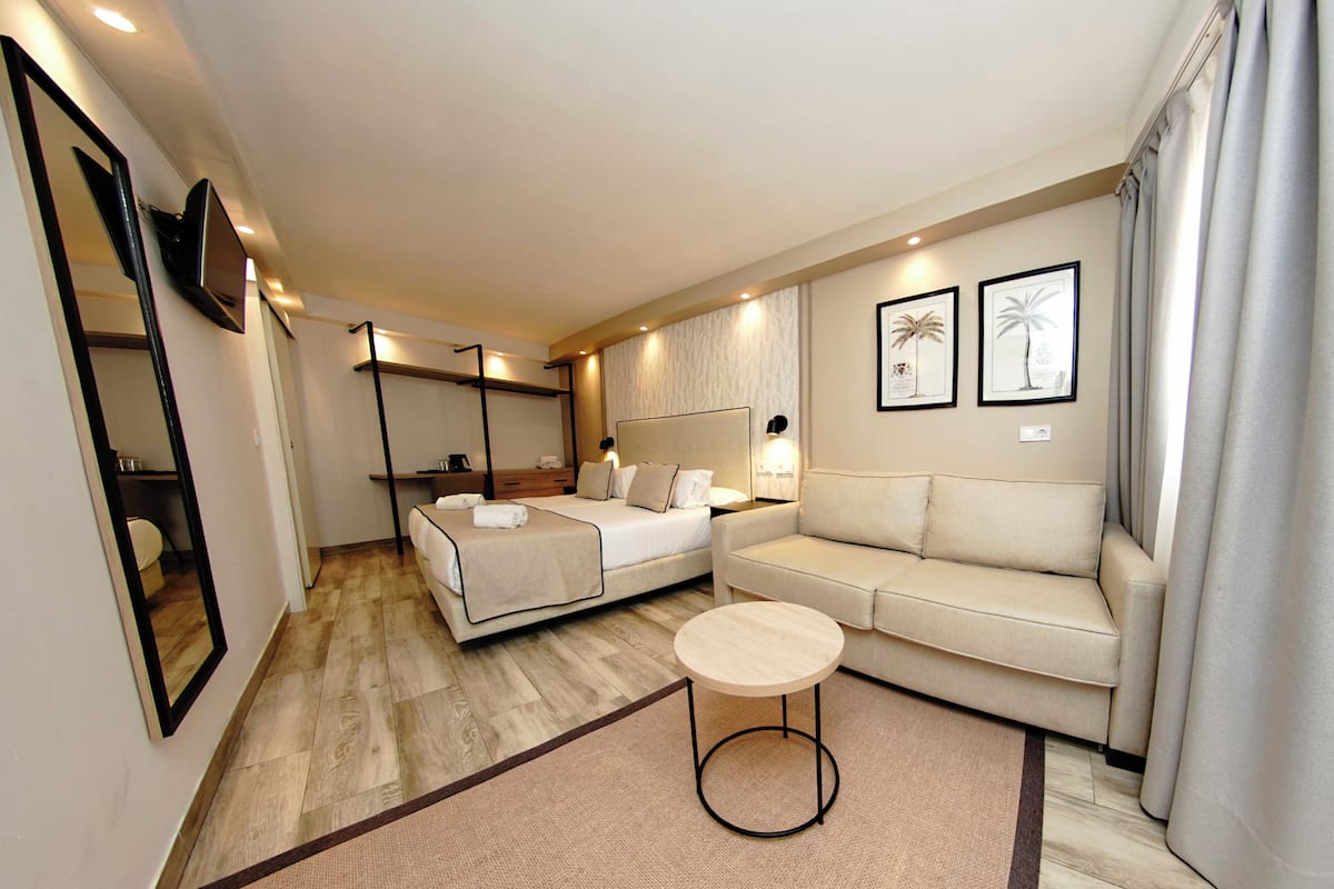 A modern hotel room with a bed, a sofa, a small round table, and a mirror.