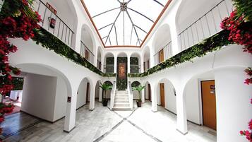 Un vaste atrium doté d’un escalier central, de murs blancs et de plantes vertes.