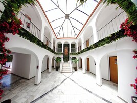 Un amplio atrio con una escalera central, paredes blancas y plantas verdes.