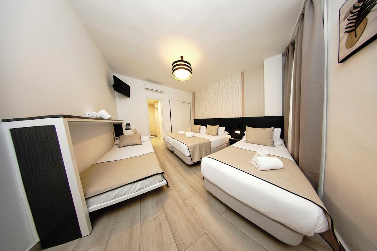 A hotel room with two single beds, a small desk, a flat-screen TV, and a ceiling light fixture.