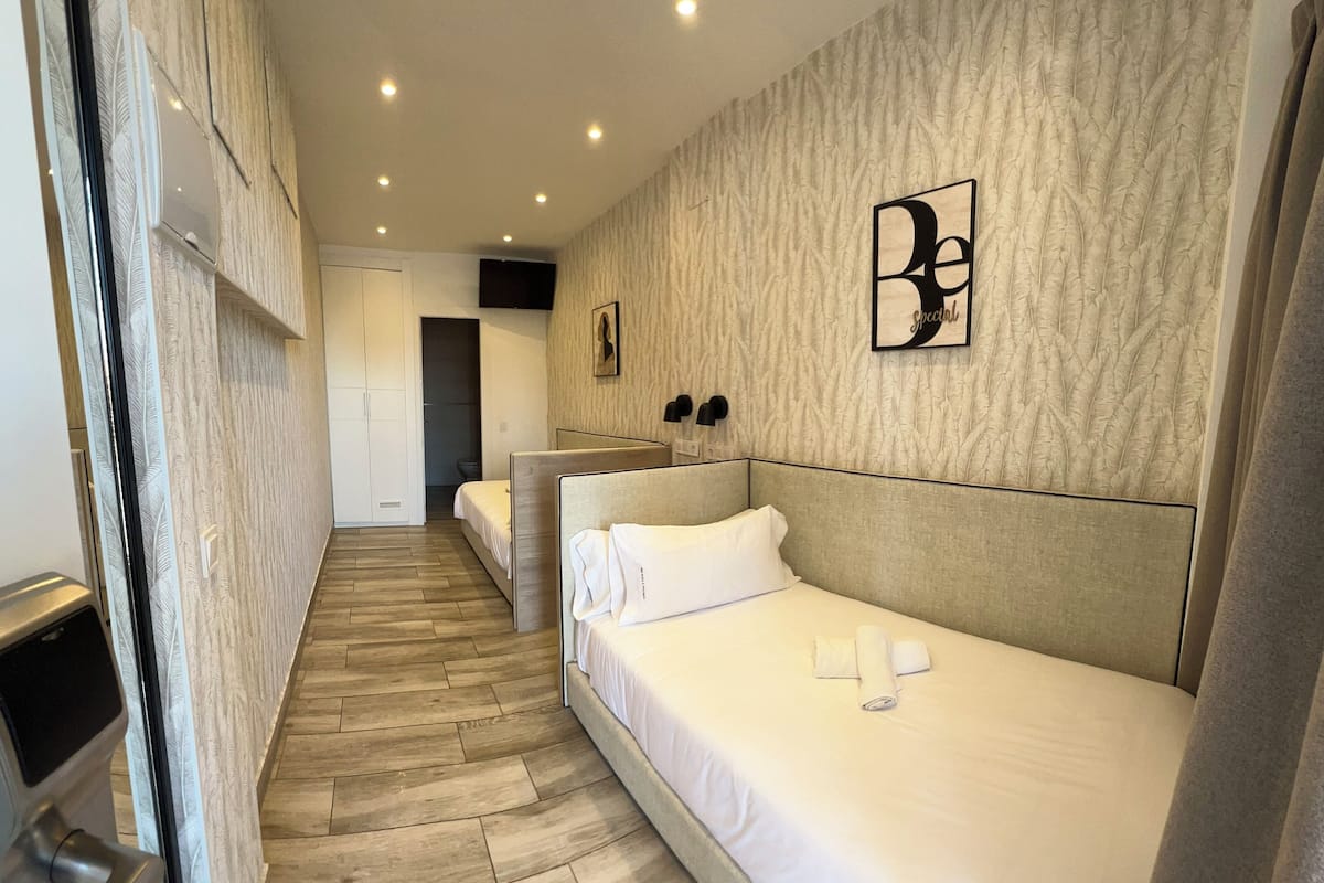 A hotel room with two single beds, a wooden floor, a textured wall, and a framed artwork.