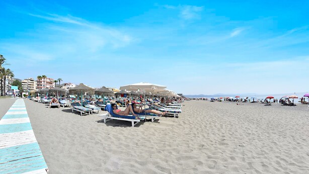 A beach with sun loungers and umbrellas, a clear sky, and buildings in the background. - Hotel Zen Airport with Free shuttle (Torremolinos)