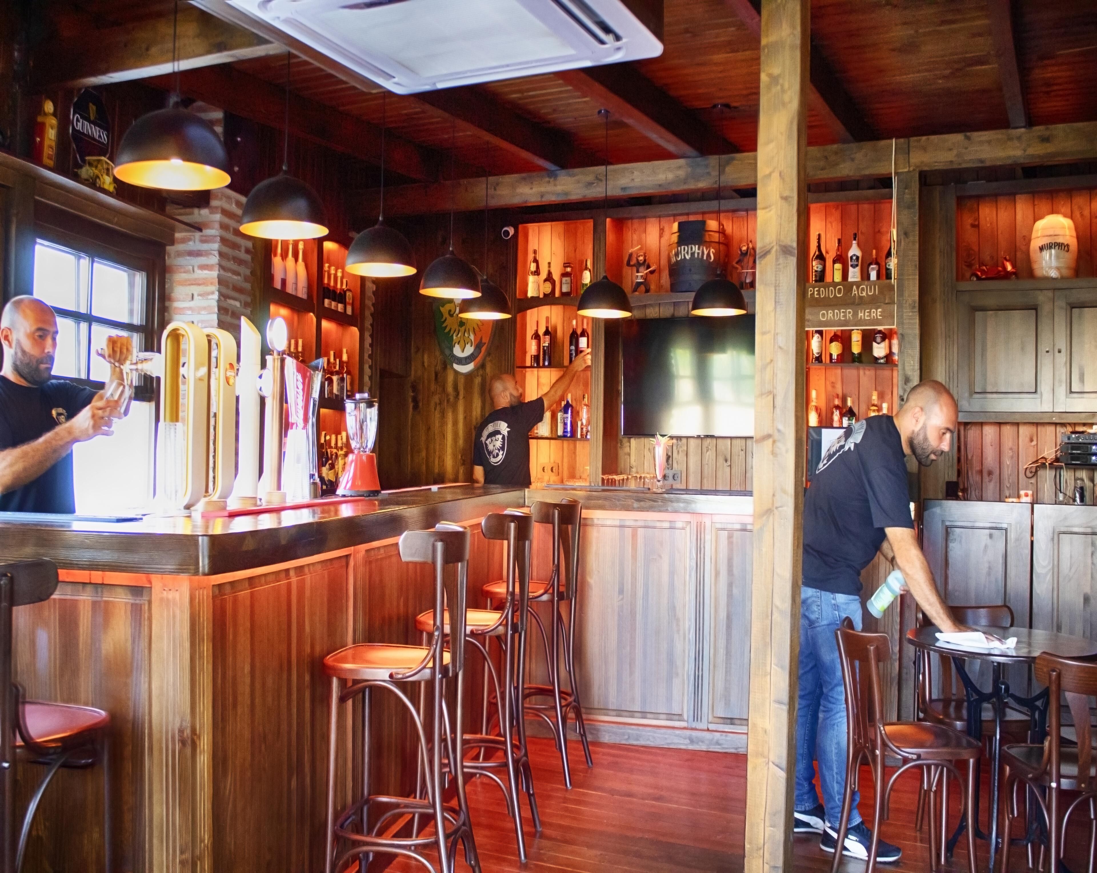 A bar with wooden interiors, bar stools, and a variety of bottles on shelves.