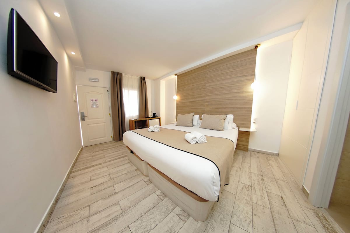 A hotel room with a large bed, a flat-screen TV mounted on the wall, and a wooden headboard.