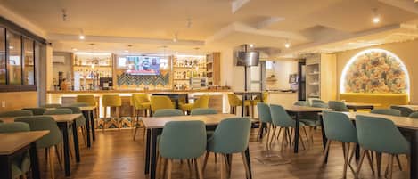 Un restaurante moderno con mesas y sillas de madera, una zona de bar y una gran pared decorativa.