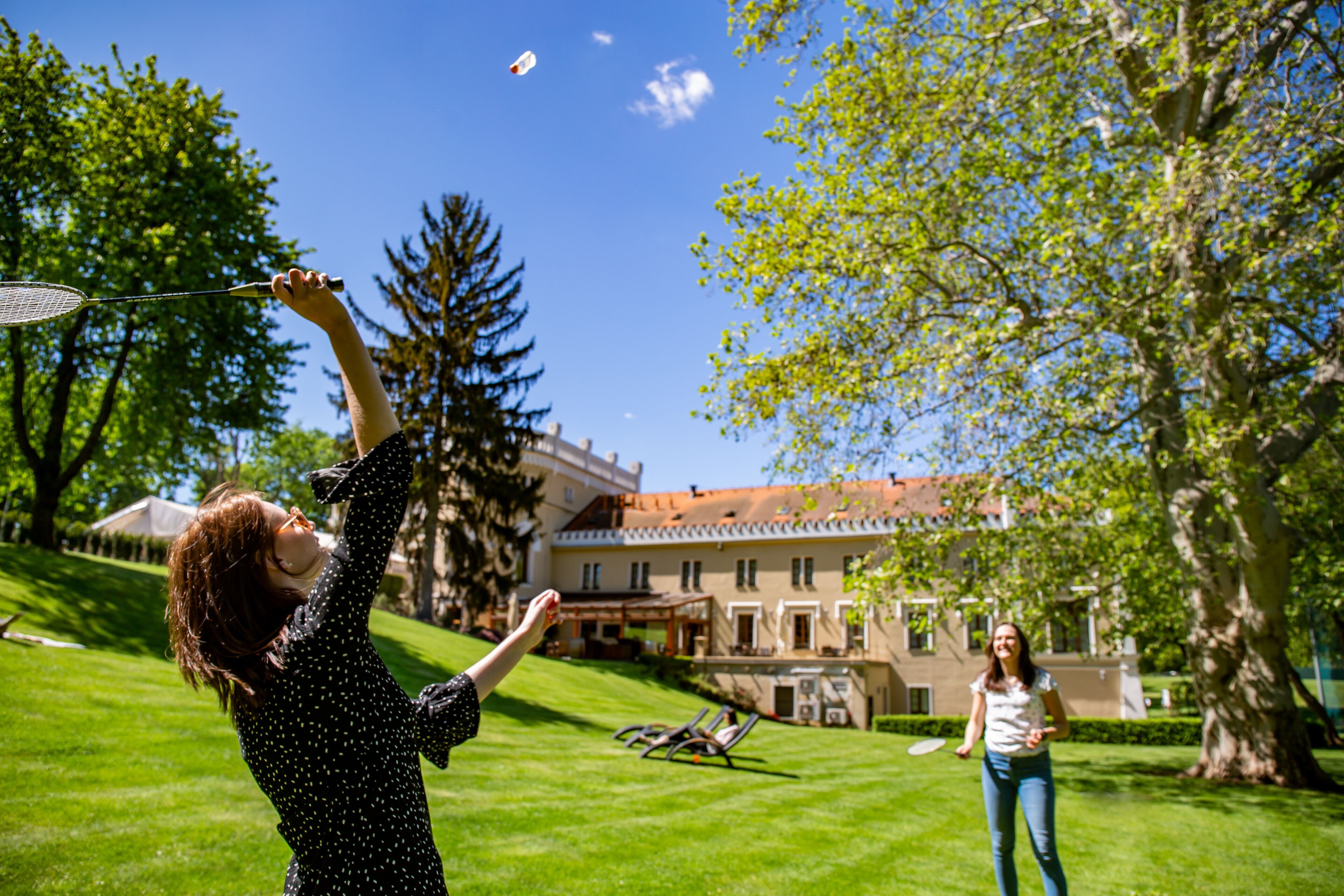A person playing badminton in a grassy area with a building in the background.