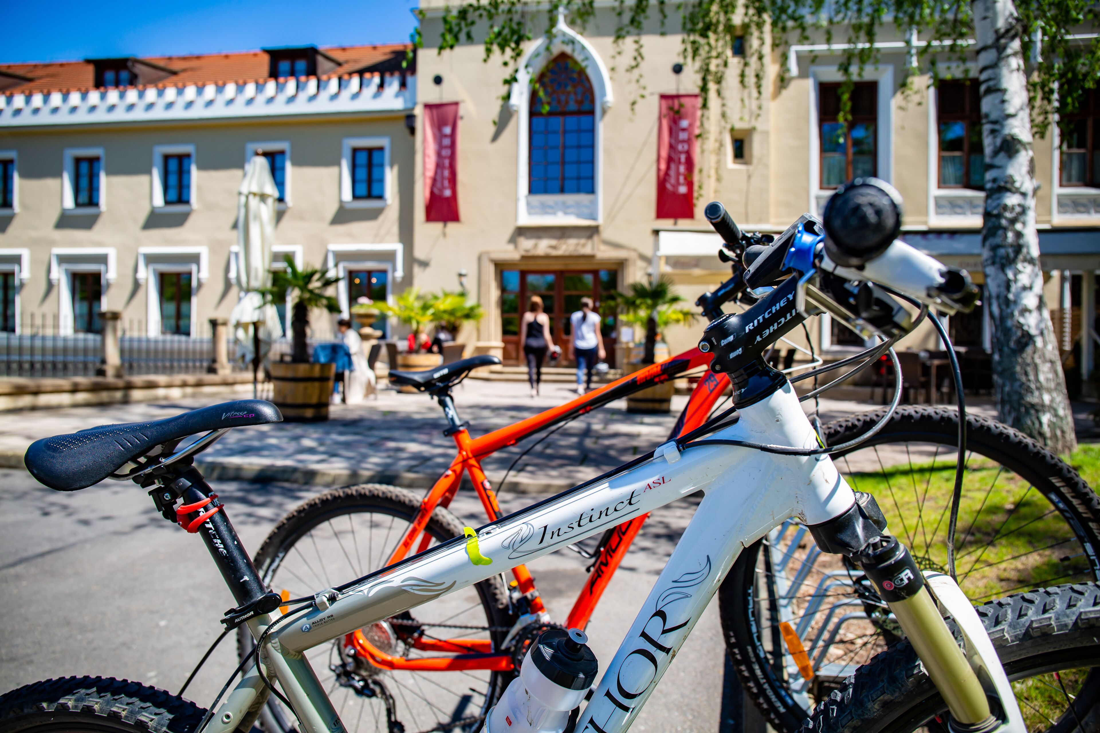 A mountain bike with a water bottle and a front suspension fork, parked in front of a building with a red awning and a large window.