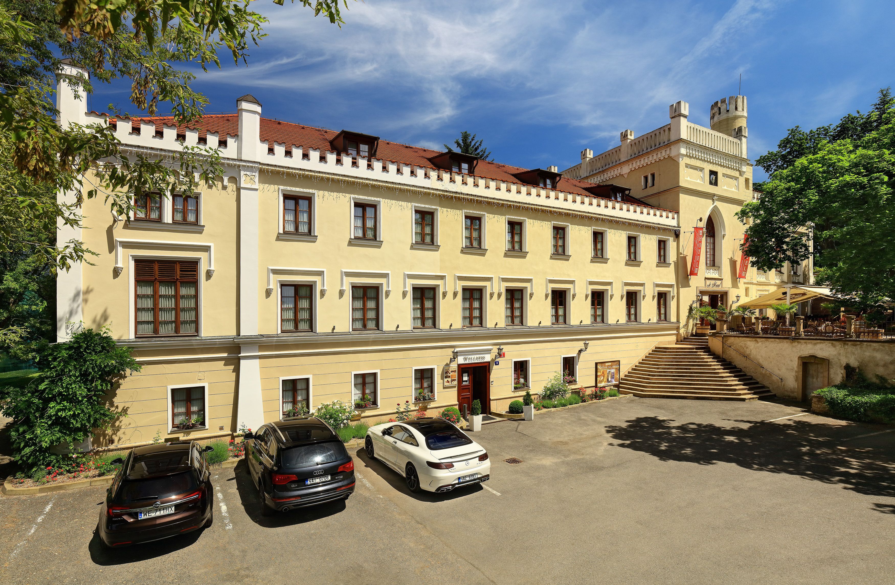 A historic building with a central courtyard, a staircase leading to the entrance, and three parked cars.