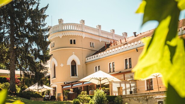 A building with a round tower, outdoor seating, and greenery. - Chateau St Havel (Prague)