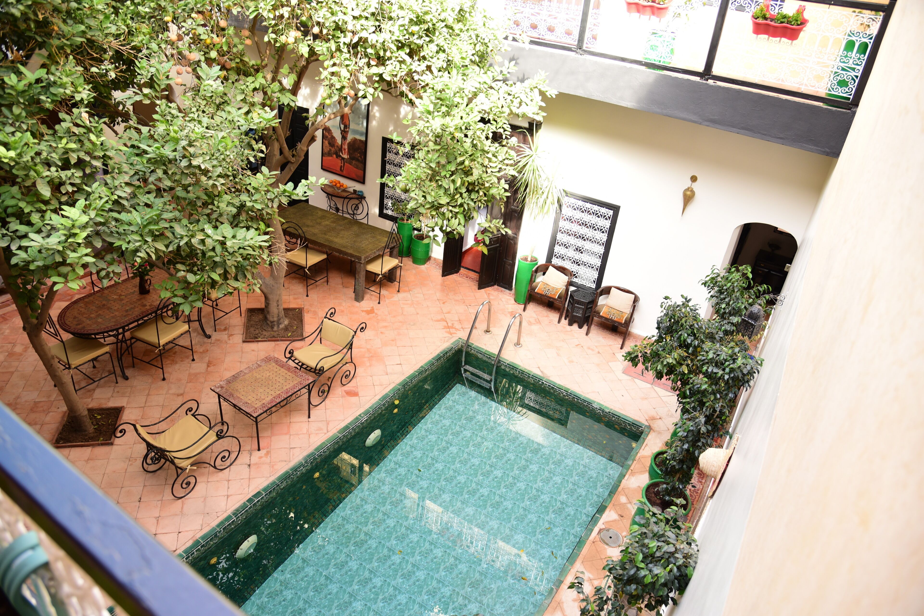 A rooftop pool area with a table and chairs, surrounded by potted plants and a view of the cityscape.