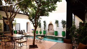 An outdoor patio with a pool, surrounded by green potted plants and a table with chairs. - Riad du Petit Prince (Marrakech)