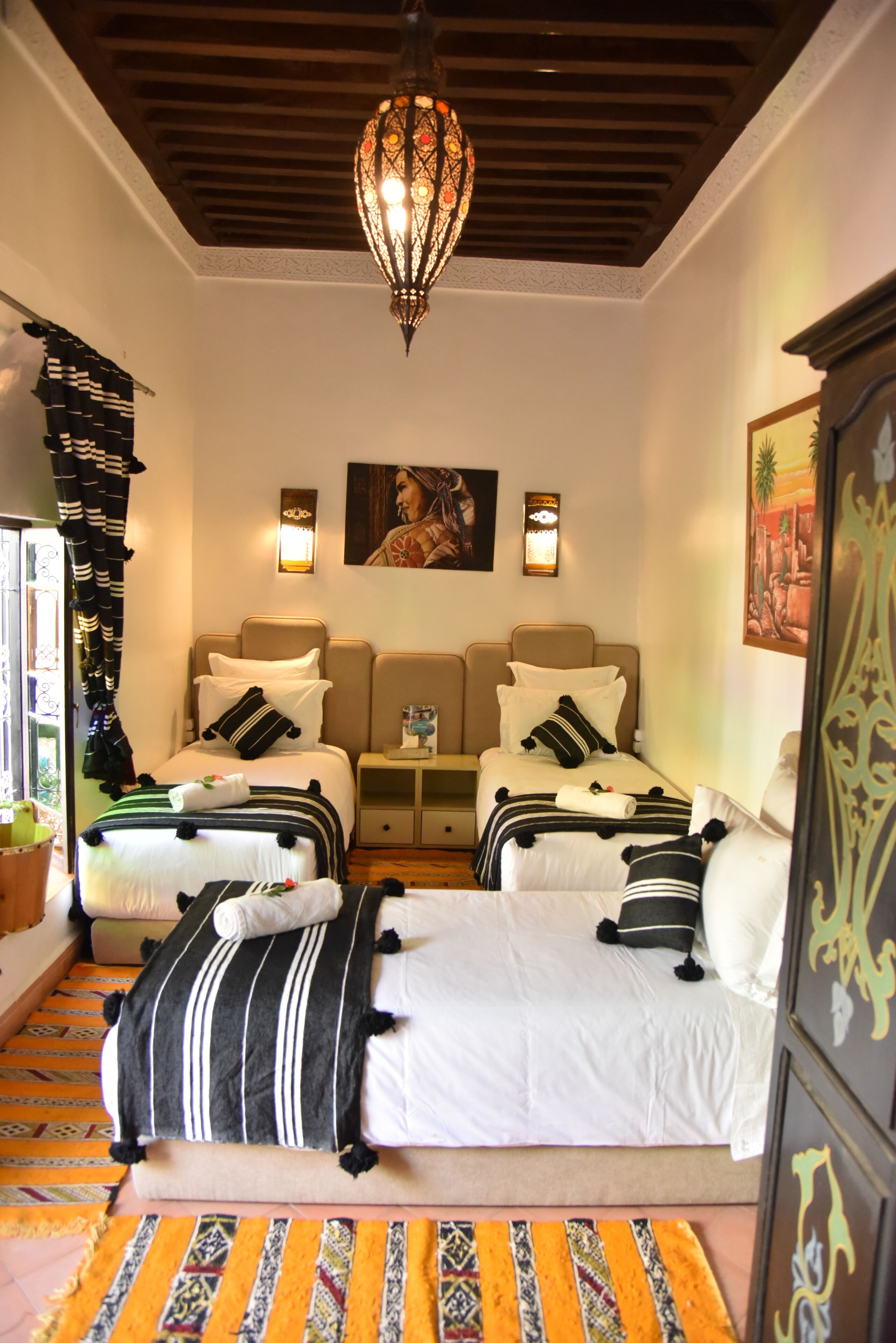 A hotel room with two beds, a chandelier, wall art, and a patterned rug.