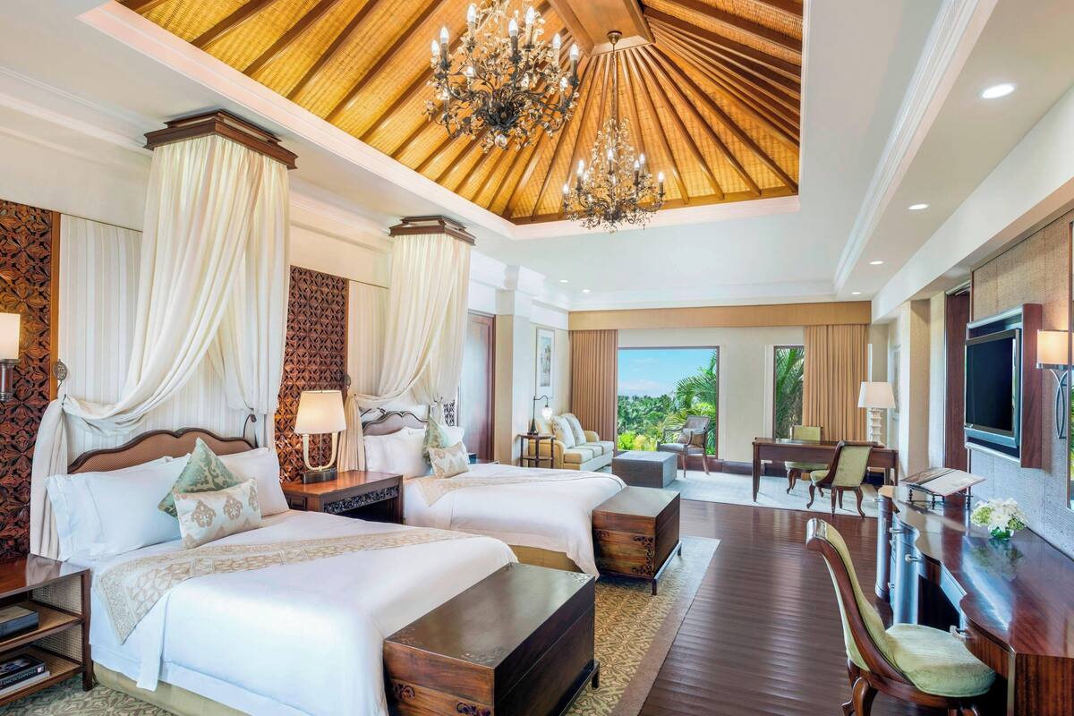 Une chambre d’hôtel spacieuse, dotée de deux lits, d’un coin repas et d’une grande fenêtre donnant sur l’extérieur.