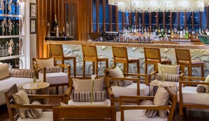 A bar area with wooden chairs and tables, a bar counter with various bottles, and a decorative wall with trophies.