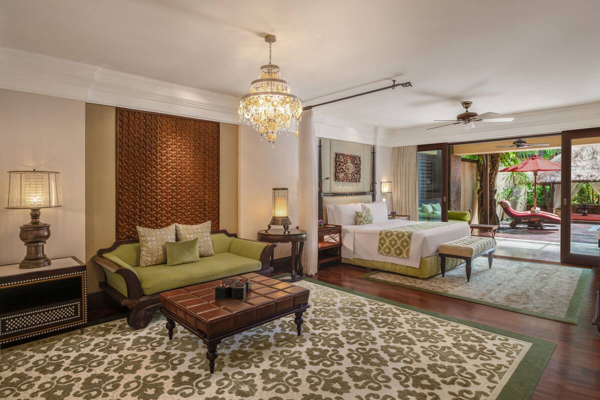 Une chambre d’hôtel spacieuse, dotée d’un grand lit, d’un canapé vert, d’une table basse en bois et d’un lustre.