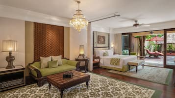 A spacious hotel room with a large bed, a green sofa, a wooden coffee table, and a chandelier.