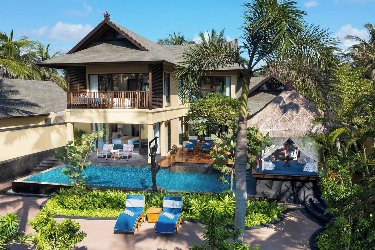 Un complexe hôtelier à deux étages doté d’une piscine, de chaises longues et d’un aménagement paysager de style tropical.