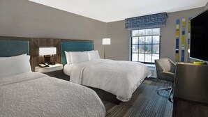 A hotel room with two beds, a desk, a chair, a lamp, and a window with a view.