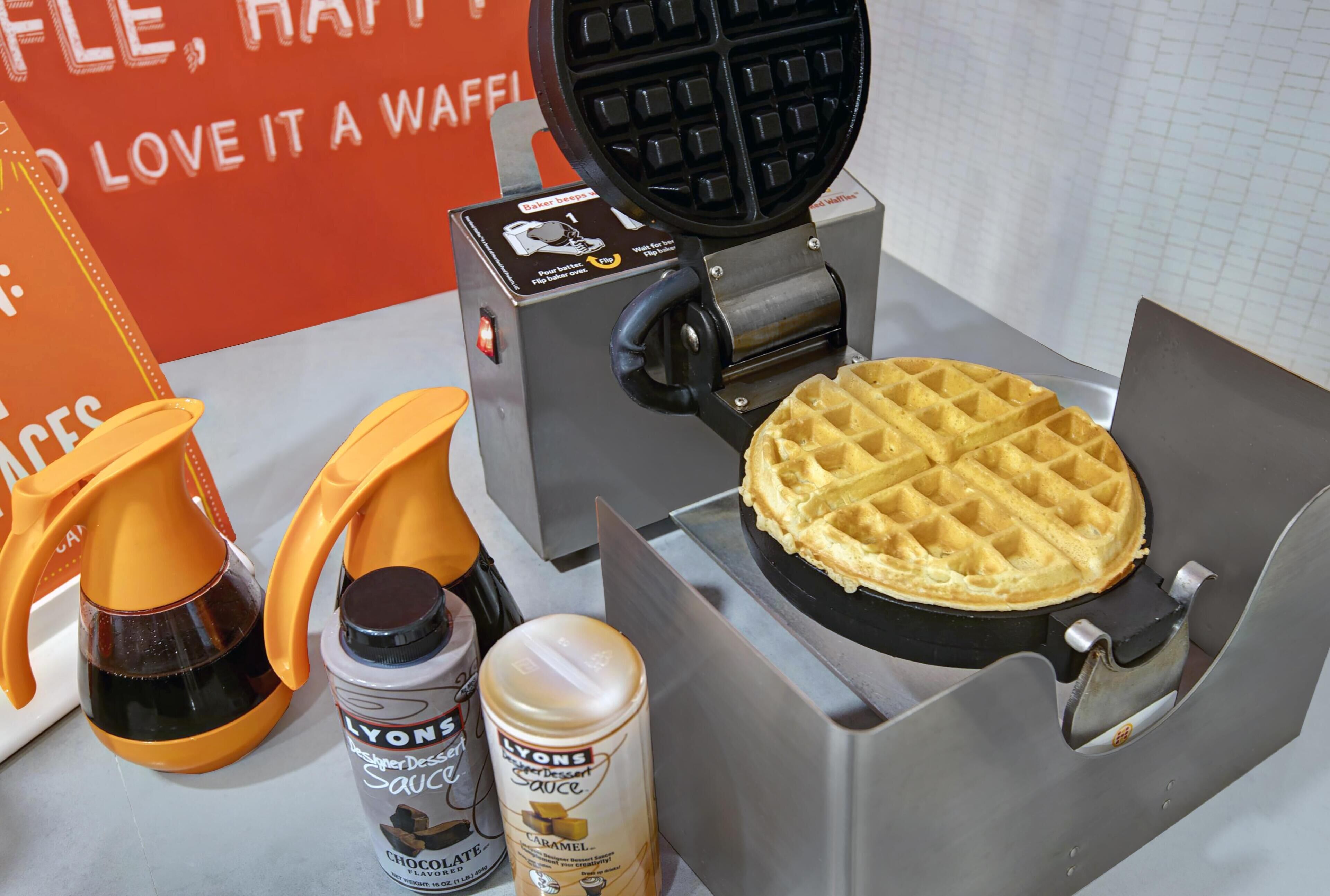 A waffle maker with a waffle, two orange squeeze bottles, and two cans of sauce.