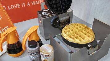 A waffle maker with a waffle, two orange squeeze bottles, and two cans of sauce.